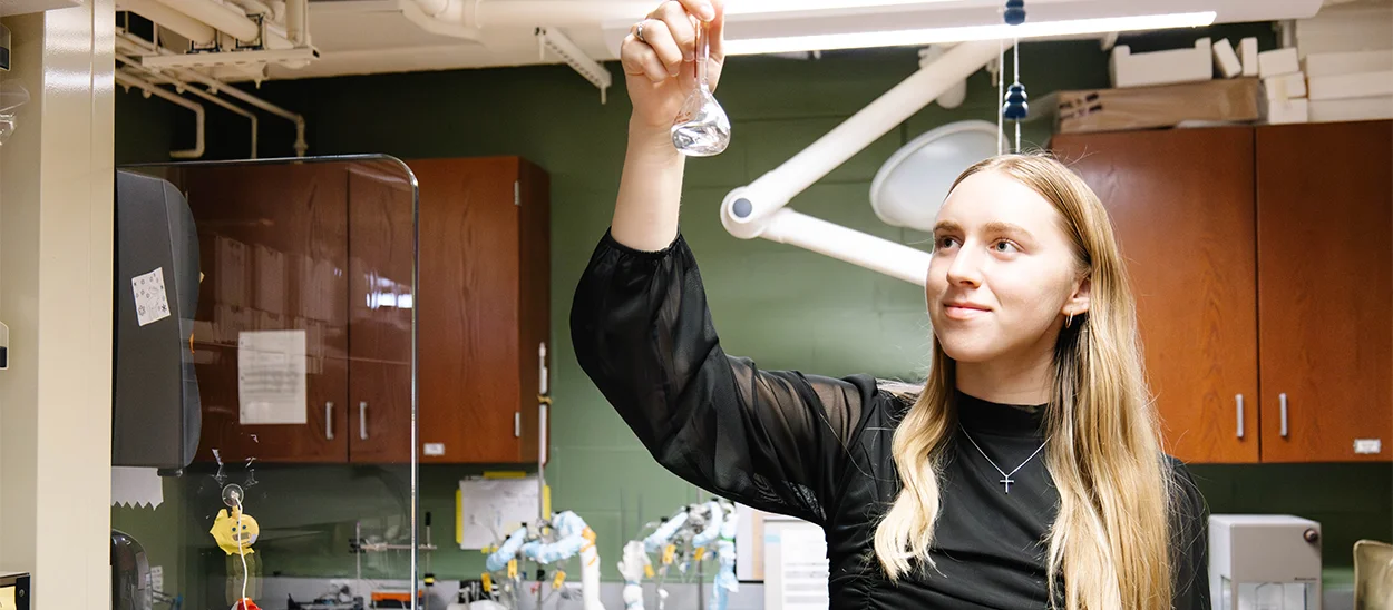 Person in a laboratory holding a small glass container, with lab equipment in the background.