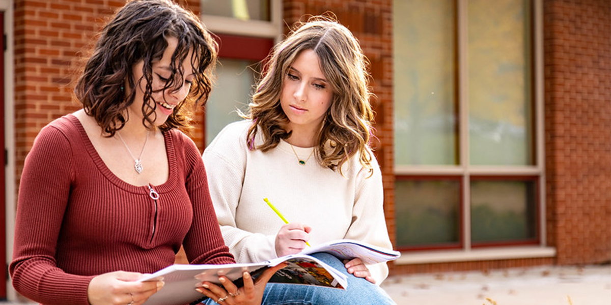 Two young women studying together outdoors, engaged in a collaborative learning session.