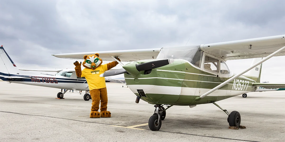 Vinny the Bearcat poses beside a small airplane used in the aviation management program