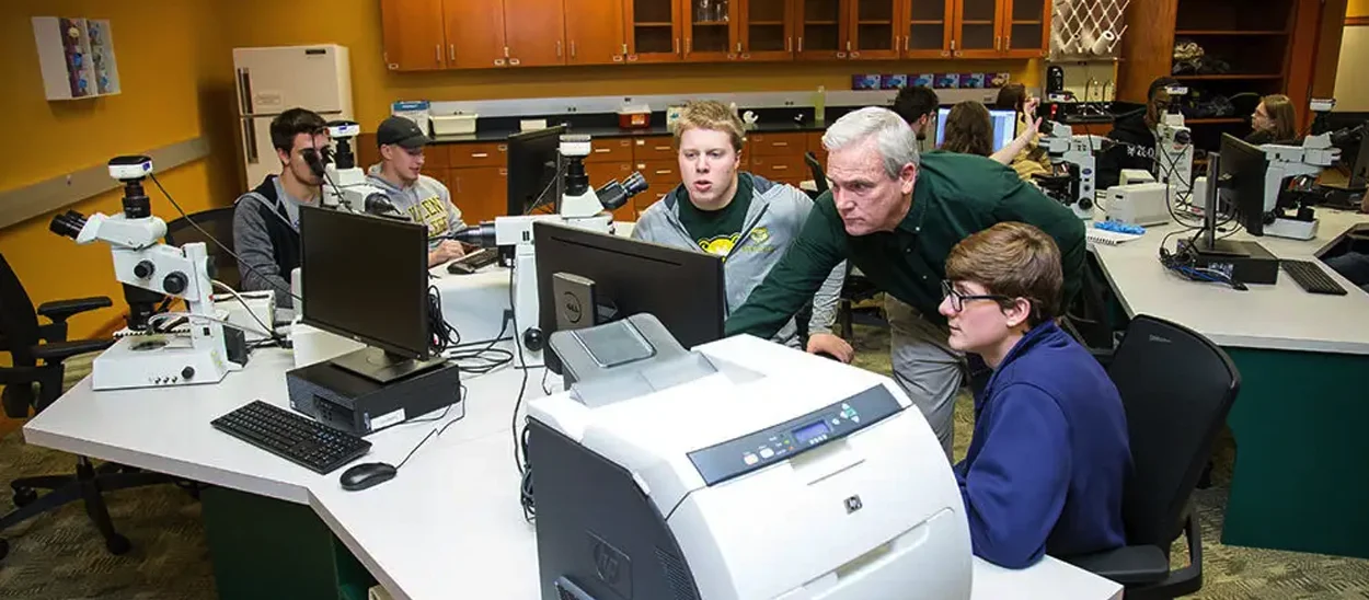 A group of students and a teacher collaborate around computers in a classroom equipped with scientific equipment.