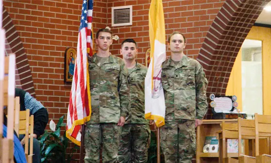 Students in military uniform standing with american flag in a classroom