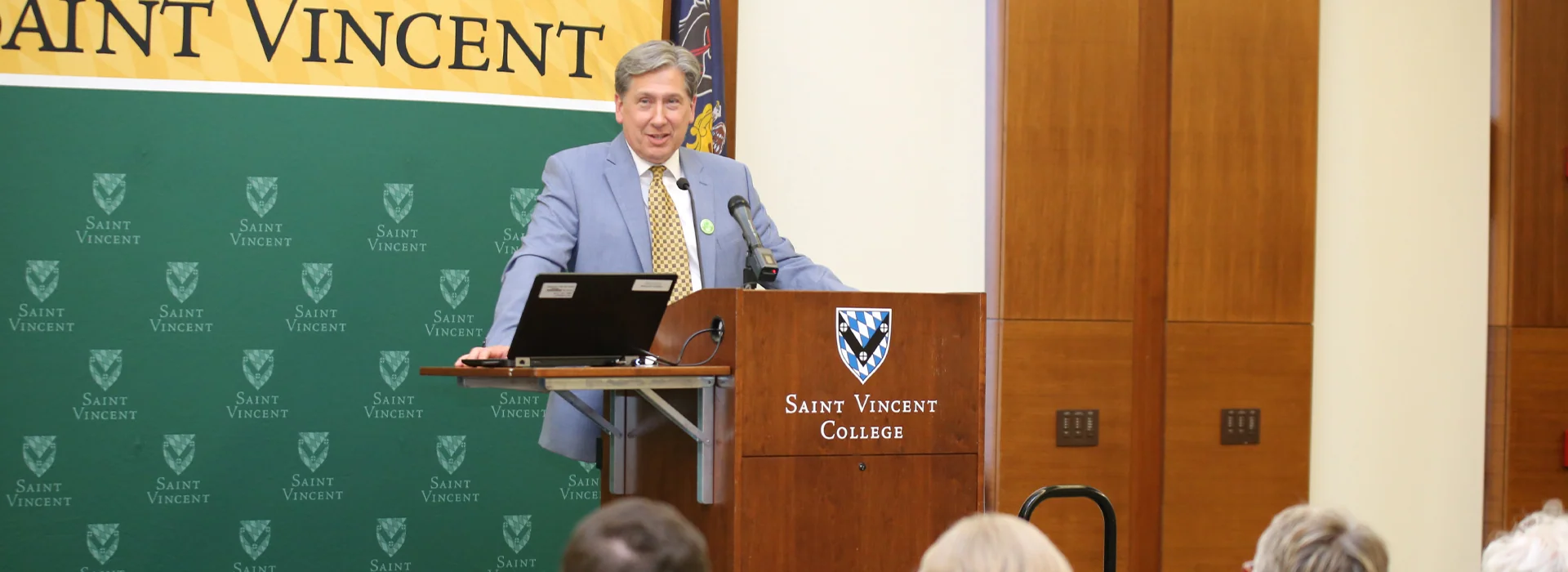 A speaker delivers a presentation at Saint Vincent College, with a banner and backdrop featuring the college's logo.