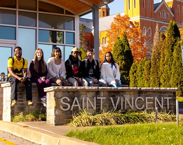 A group of six students sitting on a stone wall with the text SAINT VINCENT in front of a college campus.