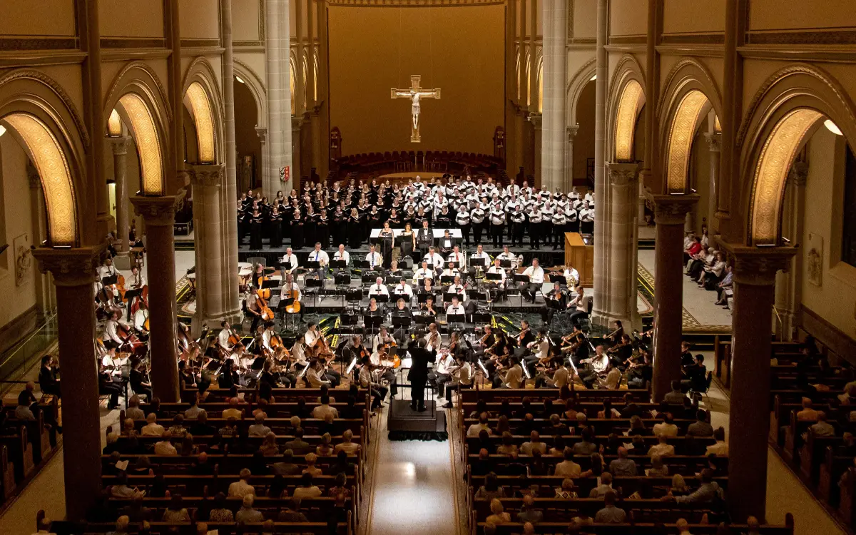 A large orchestra and choir perform in a grand church setting, creating a vibrant musical atmosphere.