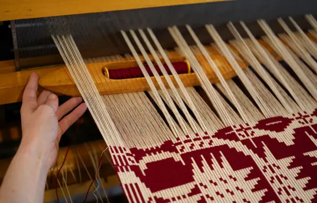 A craftsman using a loom to weave a red and white patterned textile.