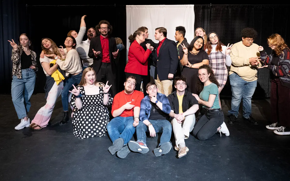 A diverse group of theater performers posing together in a playful manner for a production, showcasing both serious and comedic expressions.