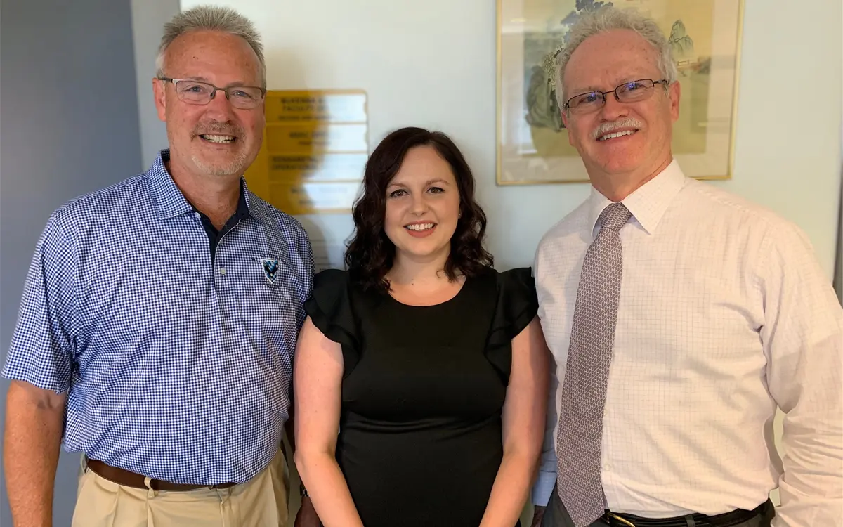 Three professionals posed together in an office setting, smiling for the camera.