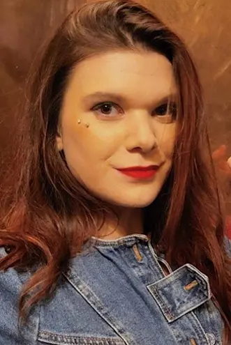 A woman with long brown hair and red lipstick poses confidently, wearing a denim jacket.