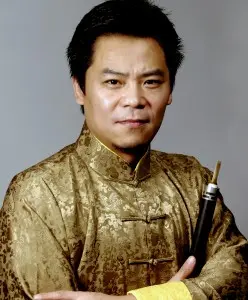 A man wearing a traditional gold-patterned Chinese outfit, confidently posing with a musical instrument.