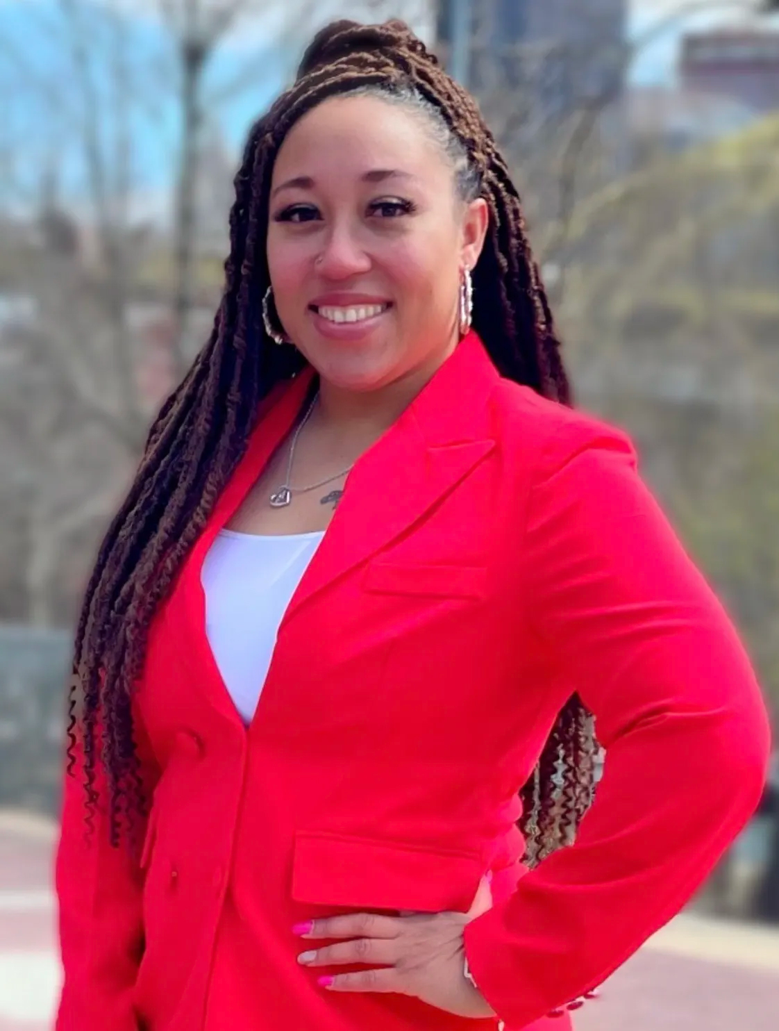 A smiling woman in a bright red suit jacket poses confidently outdoors.