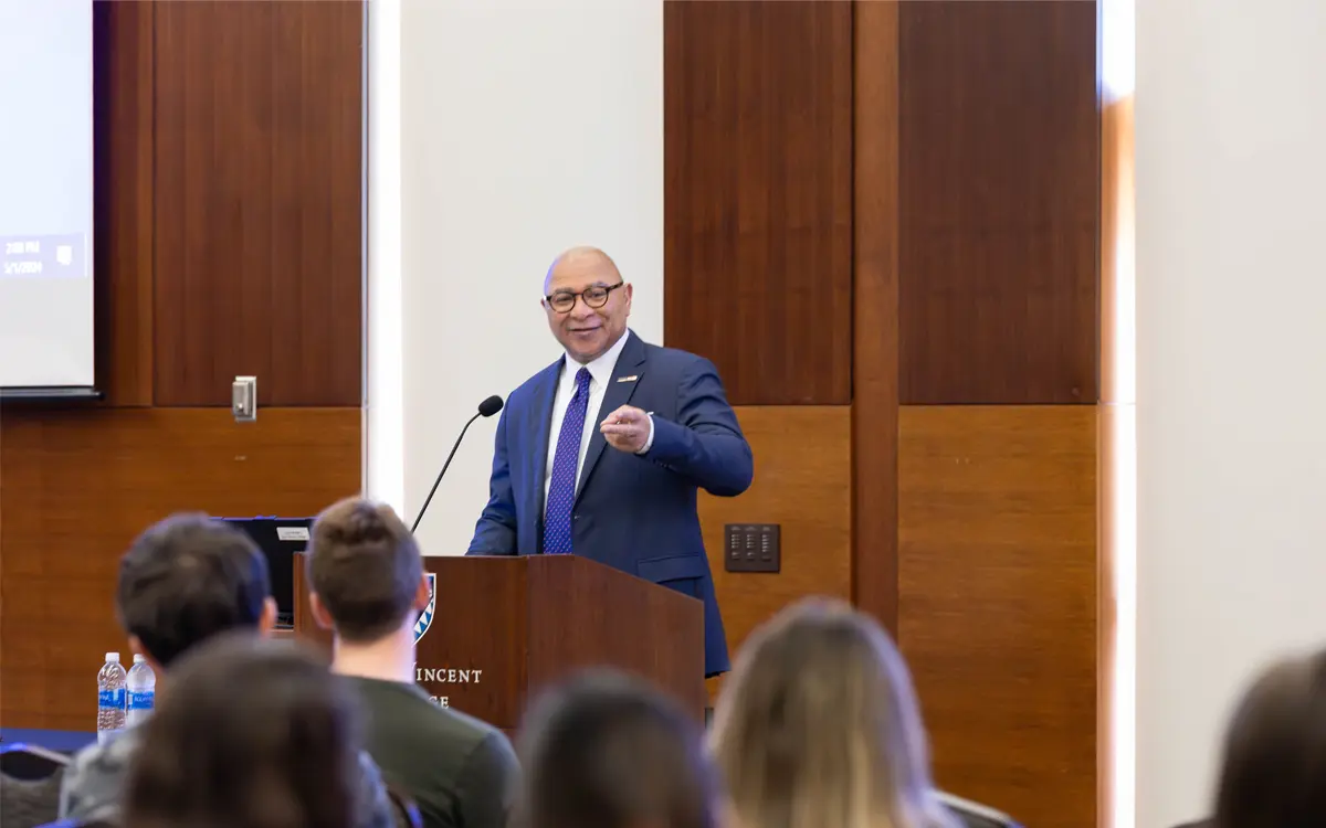 A speaker presenting at a podium with an audience in a conference setting.