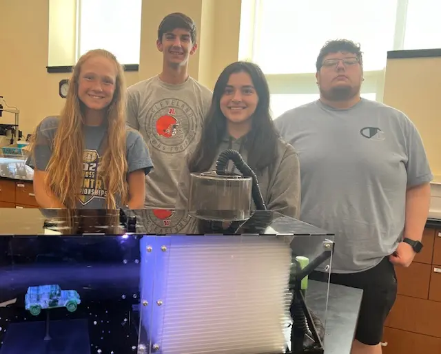 Group of four students posing in a lab, with a science project displayed in front of them.