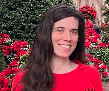 Dr. Mary Regina Boland smiles in front of vibrant red poinsettia plants.