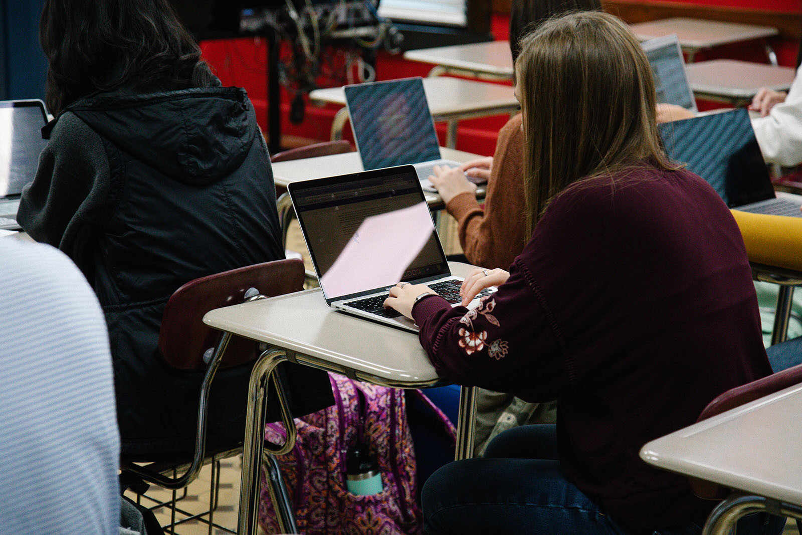 Students using laptops in a classroom setting, focused on their screens.