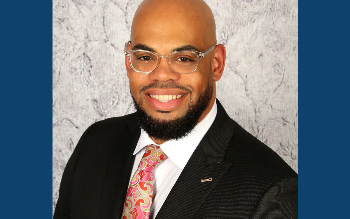 Portrait of Rev. Dr. Clarence E. Wright smiling wearing a black suit and a colorful tie with a matching pocket square.