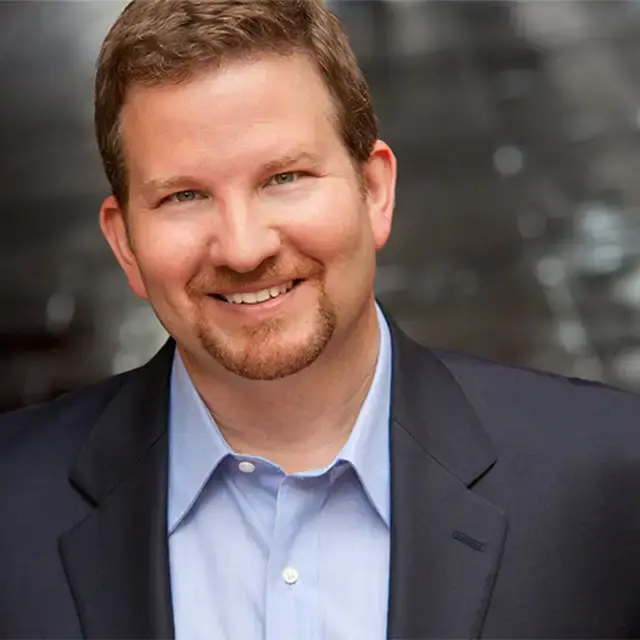 Professional headshot of a smiling man in a blazer with a light blue shirt.