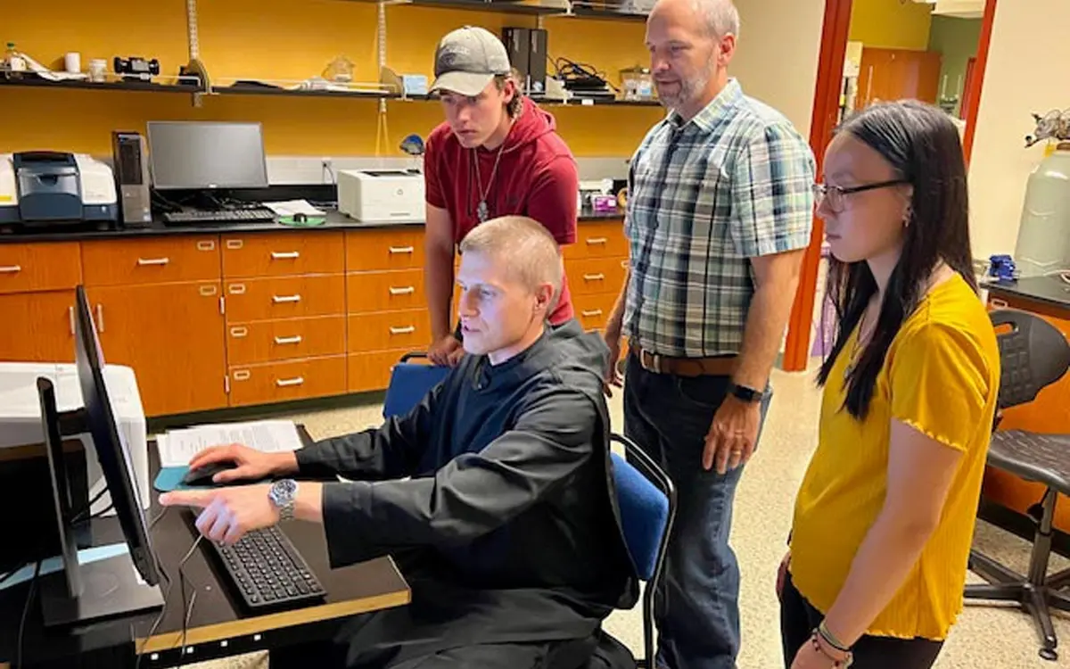 Group of four individuals collaborating around a computer in a laboratory setting.