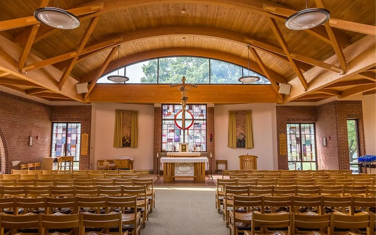 Interior view of a church with wooden beams, a central altar, and colorful stained glass windows.