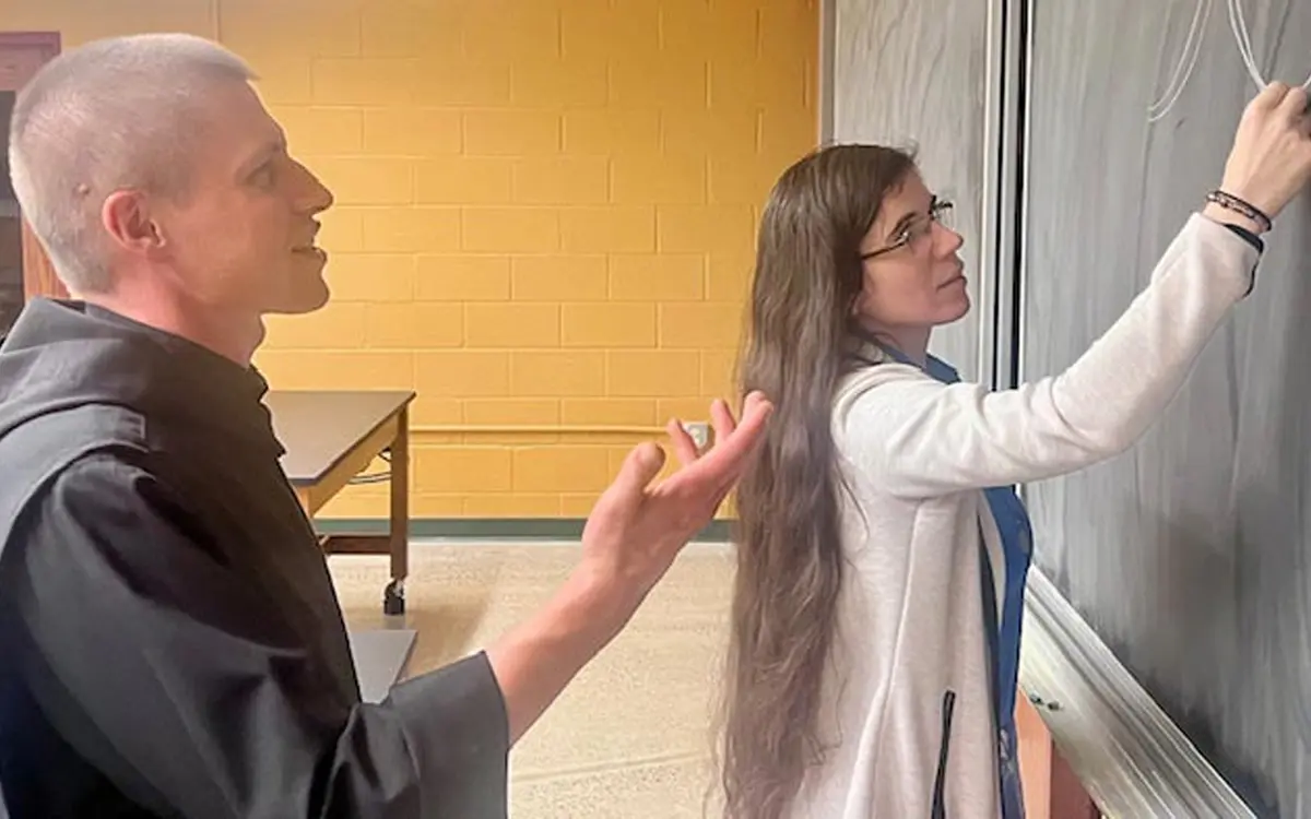 A man gestures while a woman writes on a chalkboard, indicating a collaborative teaching or brainstorming moment.