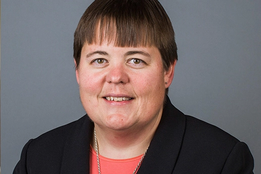 Portrait Sister Nicole Kunze in a black blazer and coral top, wearing a distinctive silver cross necklace.