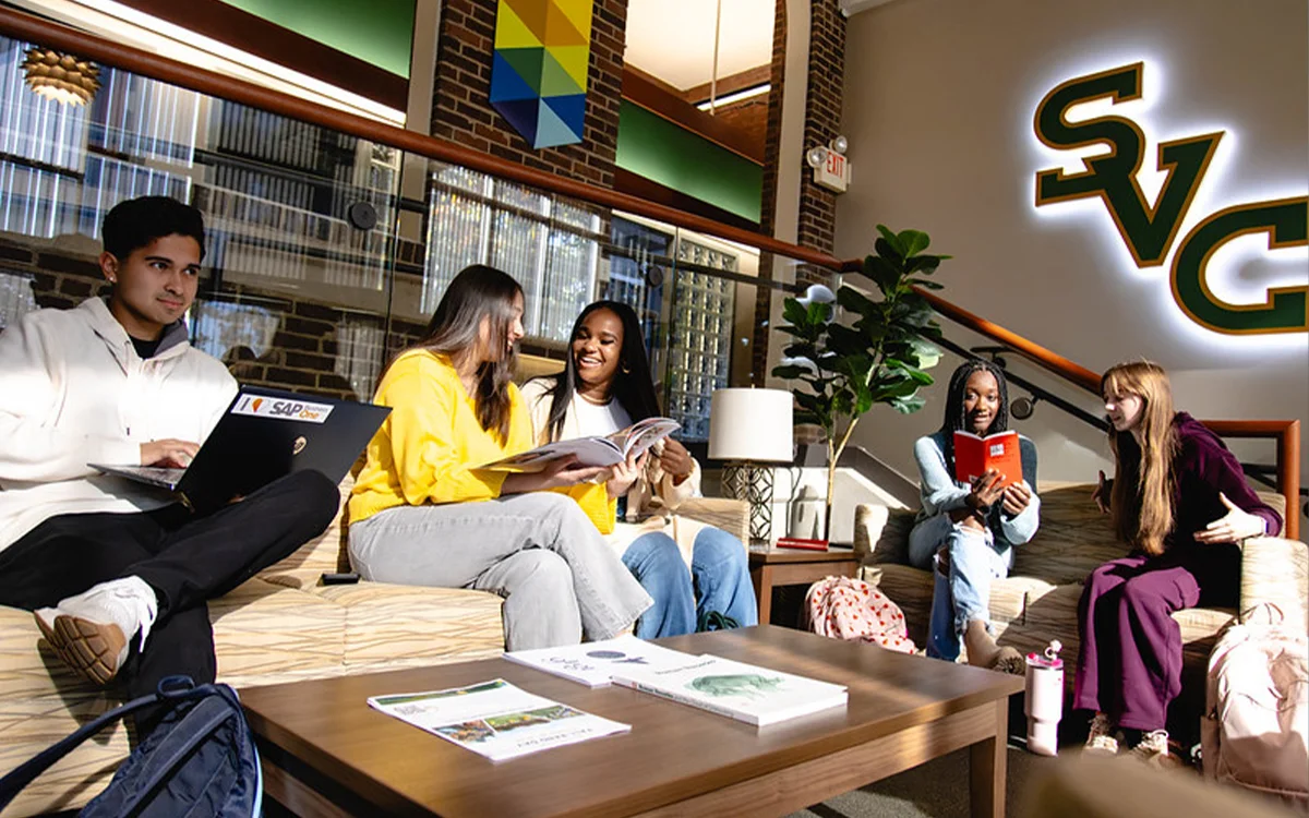 A diverse group of students collaborates and relaxes in a cozy lounge area, engaging with each other and various study materials.