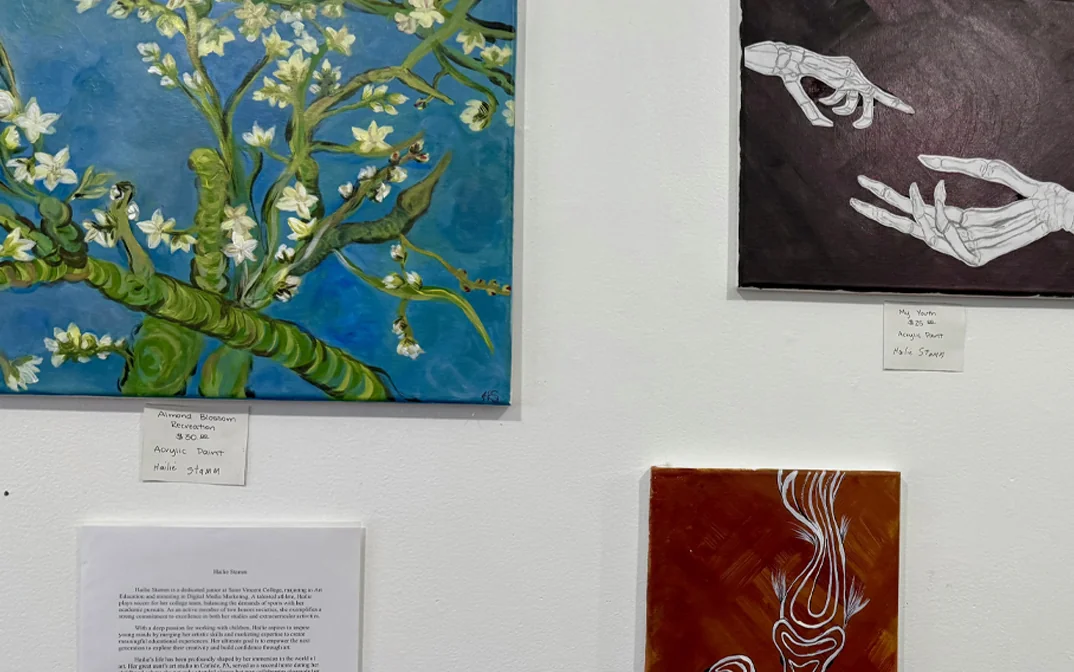 Art display featuring a vibrant painting of flowering branches, a detailed illustration of hands, and an abstract piece with warm colors.