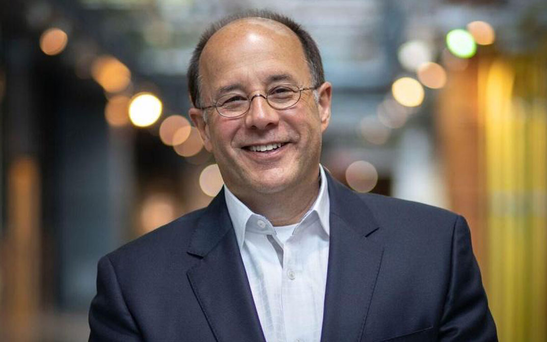 Professional headshot of a smiling man in a business suit, set in a modern indoor environment with a blurred background.